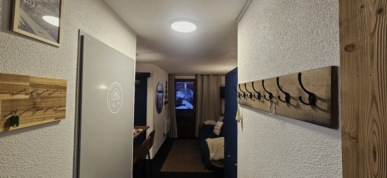Couloir d'entrée avec crochets muraux, vue vers le salon et la porte-fenêtre